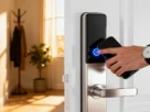Mão encostando smartphone em uma fechadura eletrônica moderna instalada em porta branca residencial.